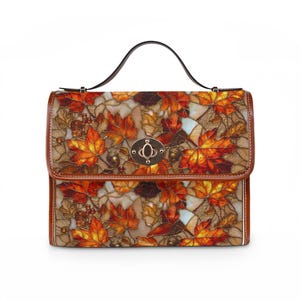 May include: A structured handbag featuring a stained glass-style print of autumn maple leaves and acorns in shades of orange, red, and brown. The bag has a brown leather-look trim, a single top handle, and a central metallic turn-lock closure.