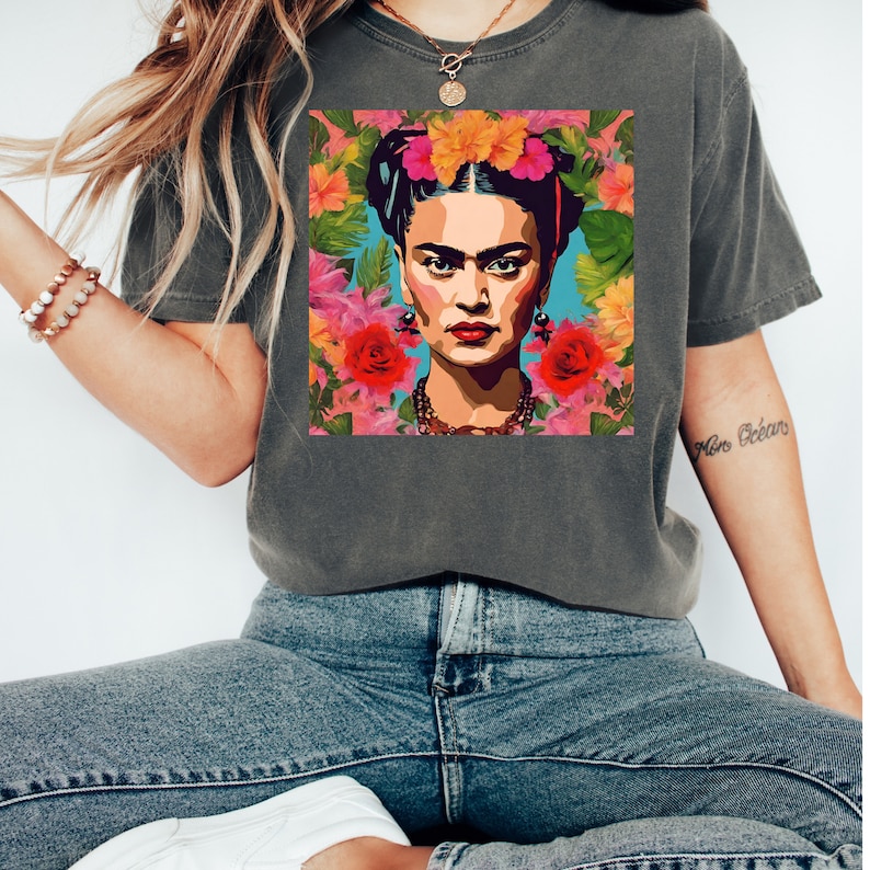May include: A dark gray t-shirt with a colorful graphic print of Frida Kahlo surrounded by flowers.
