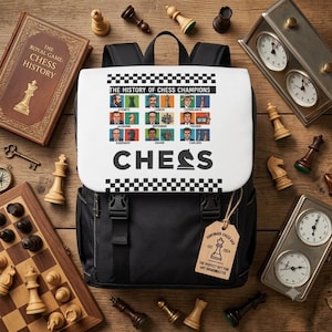 Puede incluir: Una mochila negra con una solapa blanca con borde a cuadros, el texto THE HISTORY OF CHESS CHAMPIONS, retratos de ajedrecistas y la palabra CHESS con un icono de caballo. Una etiqueta rectangular de madera cuelga de la correa frontal.