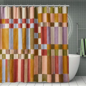 May include: A shower curtain featuring a geometric grid pattern with vertical and horizontal bands in shades of terracotta, mustard yellow, olive green, light blue, and soft pink, suspended from a series of silver metal rings along the top edge.