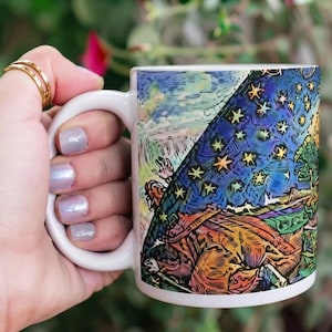 May include: A white ceramic mug featuring a vibrant, multi-colored graphic print that depicts a stylized scene with a starry night sky, a large figure, and intricate line work. The design covers the side of the mug, showcasing deep blues, oranges, and greens in a detailed, illustrative art style.