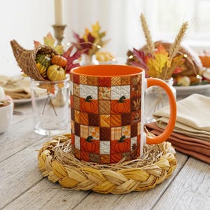 Peut inclure: Un mug en céramique avec une anse et un intérieur orange, orné d'un motif de patchwork sur l'extérieur. Le design présente des carrés avec des citrouilles orange, des feuilles d'automne, des textures écossaises et des tons bruns sur fond blanc.