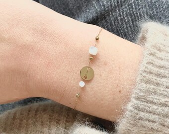 Puede incluir: Un brazalete de cadena dorada con cuentas blancas y un dije dorado con un diseño de llave.