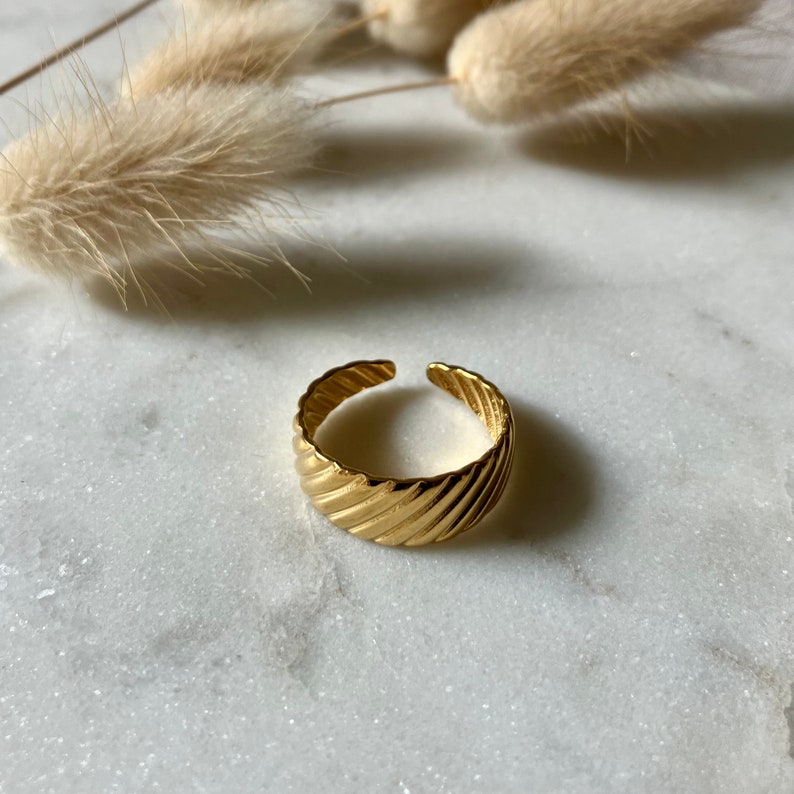 K&ouml;nnte beinhalten: Ein verstellbarer Ring in Goldton mit einem strukturierten, geriffelten Design. Der Ring ist aus Metall und hat einen schlichten, modernen Stil.
