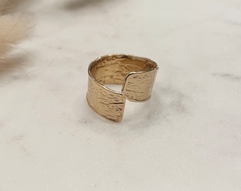 May include: A gold-toned ring with a textured, hammered finish. The ring is open and adjustable, making it a versatile piece of jewelry.