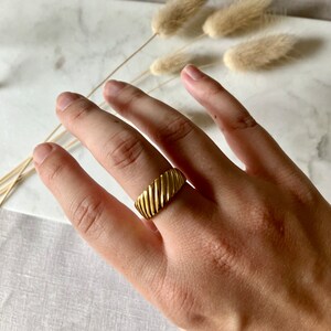 K&ouml;nnte beinhalten: Ein goldfarbener Ring mit einem strukturierten, gerippten Design. Der Ring wird an einem Finger getragen.