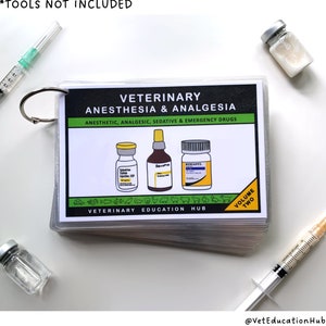 May include: A stack of flashcards for veterinary anesthesia and analgesia, held together by a silver ring. The cover features the title, "VETERINARY ANESTHESIA & ANALGESIA" and illustrations of medicine bottles. Syringes and vials are scattered around the cards.
