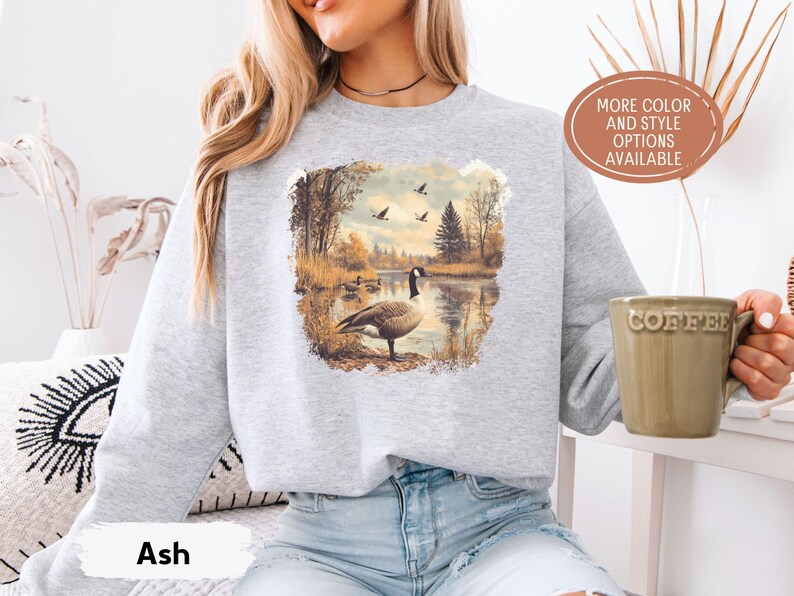 Retro fall scene with a goose by the lake and geese flying overhead, printed on a cozy 90s-style nature crewneck sweatshirt or unisex t-shirt, perfect for bird lovers and wildlife gift giving