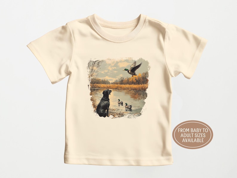 Retro duck hunting t-shirt featuring a black lab and mallard ducks by a pond, printed outdoors scene for babies, kids, and adults, perfect for hunting families and dog lovers.