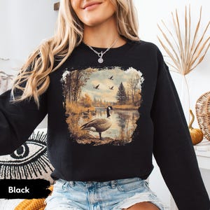 Retro fall scene with a goose by the lake and geese flying overhead, printed on a cozy 90s-style nature crewneck sweatshirt or unisex t-shirt, perfect for bird lovers and wildlife gift giving
