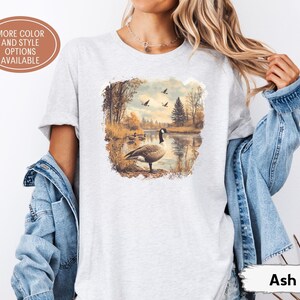 Retro fall scene with a goose by the lake and geese flying overhead, printed on a cozy 90s-style nature crewneck sweatshirt or unisex t-shirt, perfect for bird lovers and wildlife gift giving