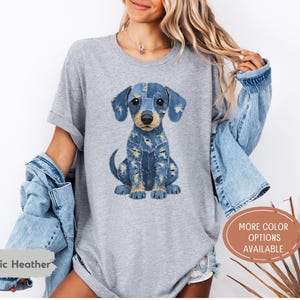 May include: Athletic heather gray t-shirt featuring a sitting dachshund dog illustration made of denim. The dog has blue denim patches and a brown nose. The shirt also has the text "More Color Options Available".
