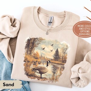 Retro fall scene with a goose by the lake and geese flying overhead, printed on a cozy 90s-style nature crewneck sweatshirt or unisex t-shirt, perfect for bird lovers and wildlife gift giving