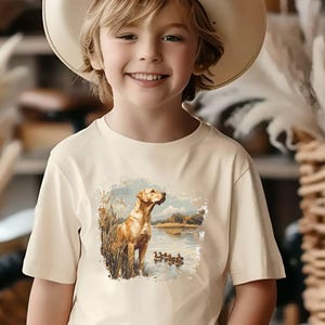 Retro duck hunting t-shirt featuring a yellow lab standing by a pond watching mallard ducks, printed design available in baby, toddler, youth, and adult sizes