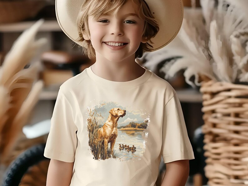 Retro duck hunting t-shirt featuring a yellow lab standing by a pond watching mallard ducks, printed design available in baby, toddler, youth, and adult sizes