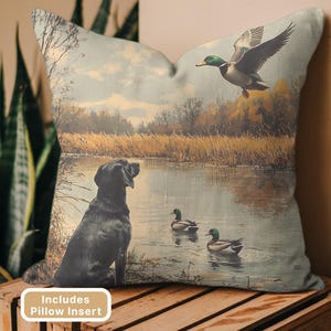 May include: Decorative pillow featuring a vintage-style illustration of a black Labrador Retriever watching ducks on a lake. A flying duck is in the air. The pillow has a neutral background and includes a pillow insert.