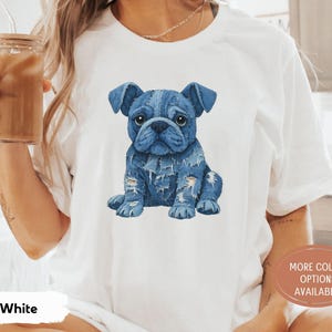 May include: White t-shirt featuring a blue watercolor illustration of a French Bulldog. The dog has a denim-like appearance with distressed details. The shirt has a round neck and short sleeves. The words "MORE COLOR OPTIONS AVAILABLE" are printed on a circular sticker.