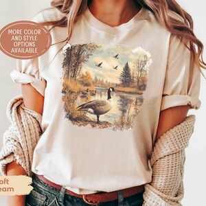 Retro fall scene with a goose by the lake and geese flying overhead, printed on a cozy 90s-style nature crewneck sweatshirt or unisex t-shirt, perfect for bird lovers and wildlife gift giving