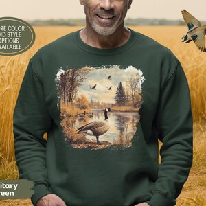 Retro fall scene with a goose by the lake and geese flying overhead, printed on a cozy 90s-style nature crewneck sweatshirt or unisex t-shirt, perfect for bird lovers and wildlife gift giving