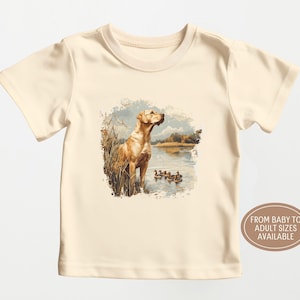 Retro duck hunting t-shirt featuring a yellow lab standing by a pond watching mallard ducks, printed design available in baby, toddler, youth, and adult sizes