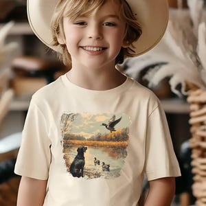Retro duck hunting tshirt featuring a black lab and mallard ducks by a pond, printed outdoors scene for babies, kids, and adults, perfect for hunting families and dog lovers.