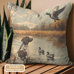 May include: Decorative pillow featuring a vintage-style hunting scene. The design includes a dog, ducks, and a lake. The pillow has a neutral color palette with a rustic aesthetic. The text "Includes Pillow Insert" is visible.