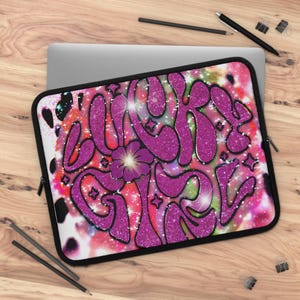 Könnte beinhalten: Eine Laptop-Hülle mit auffälligem Design. Auf der Hülle stehen die Worte "BOUJEE GIRL" in glitzerndem rosa Glitzer vor einem farbenfrohen Hintergrund aus Rosa-, Rot- und Grüntönen. Eine lila Blume ist im Design zentriert.