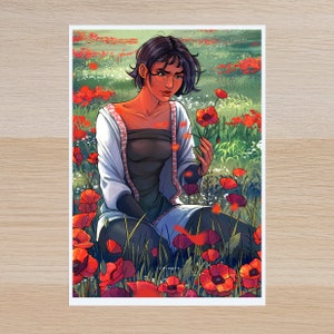 May include: A woman with dark hair and a white embroidered blouse sits in a field of red poppies. She is holding a single poppy in her hand and looking down at it.
