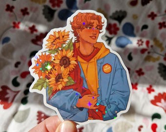 May include: A sticker featuring a cartoon illustration of a person with brown hair holding a bouquet of sunflowers. The person is wearing a blue denim jacket over a yellow hoodie. The sticker has a holographic finish.