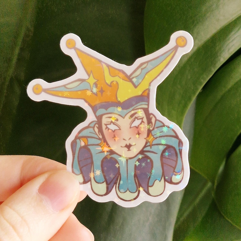 May include: A holographic sticker featuring a jester character with a yellow and blue hat, and a blue and purple outfit. The jester has a pale complexion, red blush, and a small black smile. The sticker has a white border.