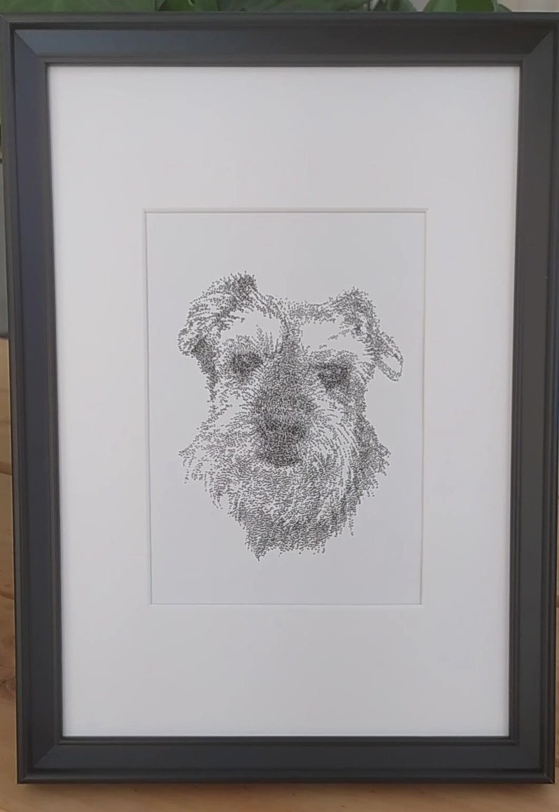 May include: A black framed print of a dog's face, drawn in a stippled style using tiny dots.