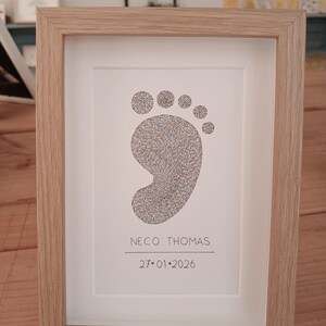 ingelijst babyvoetje gemaakt met handgeschreven woorden. Onder het voetje staat de naam en de geboortedatum van de baby.