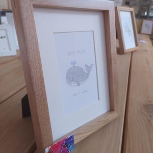 View from the left of a framed image of a baby whale. The complete image consists entirely of handwritten words. In this image the words are hundreds of times the name of the newborn baby.
Under the baby whale is written the date of the baptism.