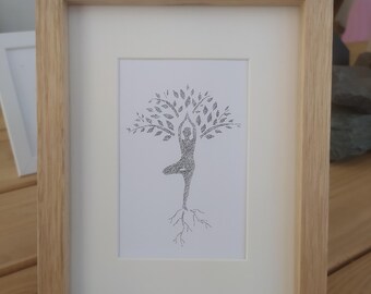 May include: A framed black and white line drawing of a person in a yoga pose, forming the shape of a tree with roots and leaves. The drawing is on white paper and is framed in a light wood frame.