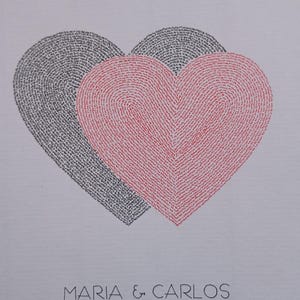 Op de afbeelding: Een witte print met twee overlappende harten, één in zwart en één in rood, beide opgebouwd uit kleine, herhalende tekst. Onder de harten staat de tekst MARIA & CARLOS, gevolgd door de datum 03*07*2025 op een aparte regel.