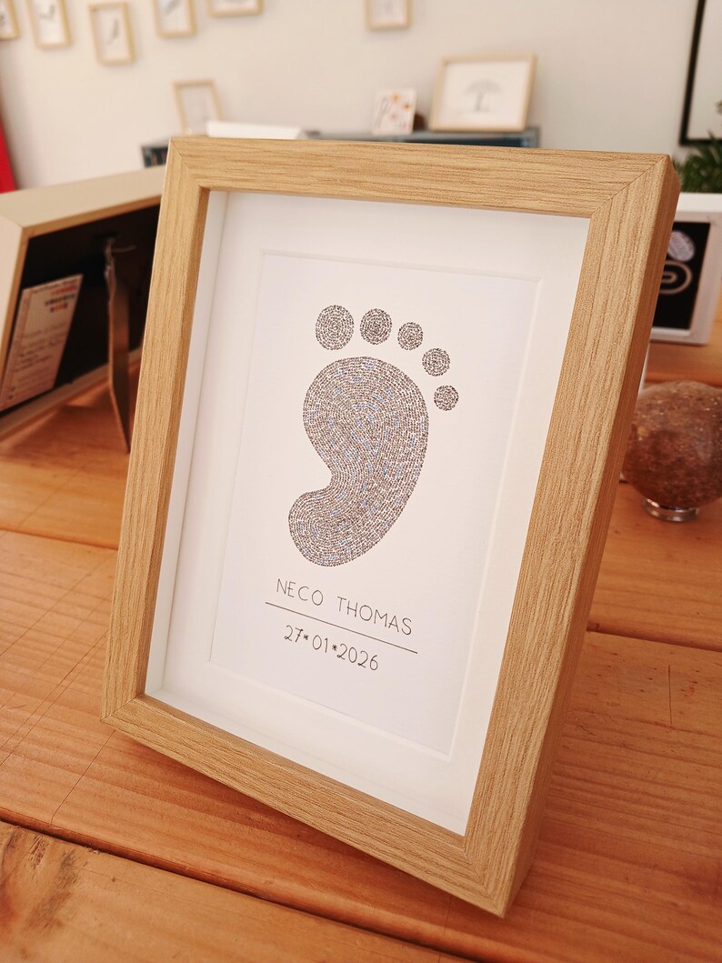 Ingelijst voorbeeld van een babyvoetje, gemaakt met handgeschreven woorden. Er onder de volledige naam van de baby en de geboortedatum.