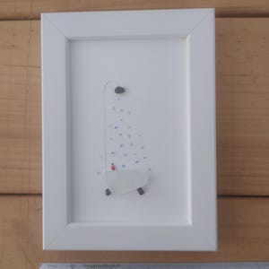 Puede incluir: Una imagen enmarcada en blanco con una bañera blanca hecha de vidrio de mar con una persona roja dentro. La bañera está debajo de una ducha hecha de vidrio de mar azul y blanco.