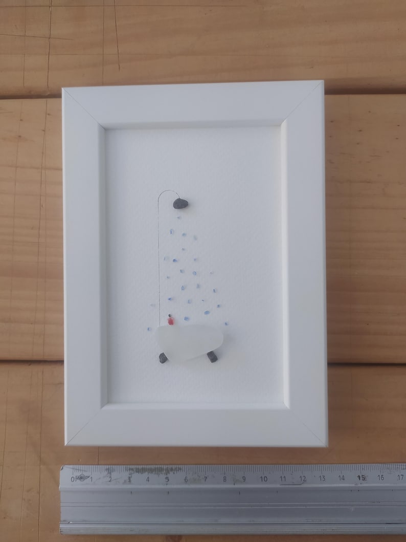 以下が含まれることがあります： 白い額縁に入った絵画。白い海ガラス製のバスタブの中に赤い人が入っています。バスタブの上には青と白の海ガラス製のシャワーがあります。