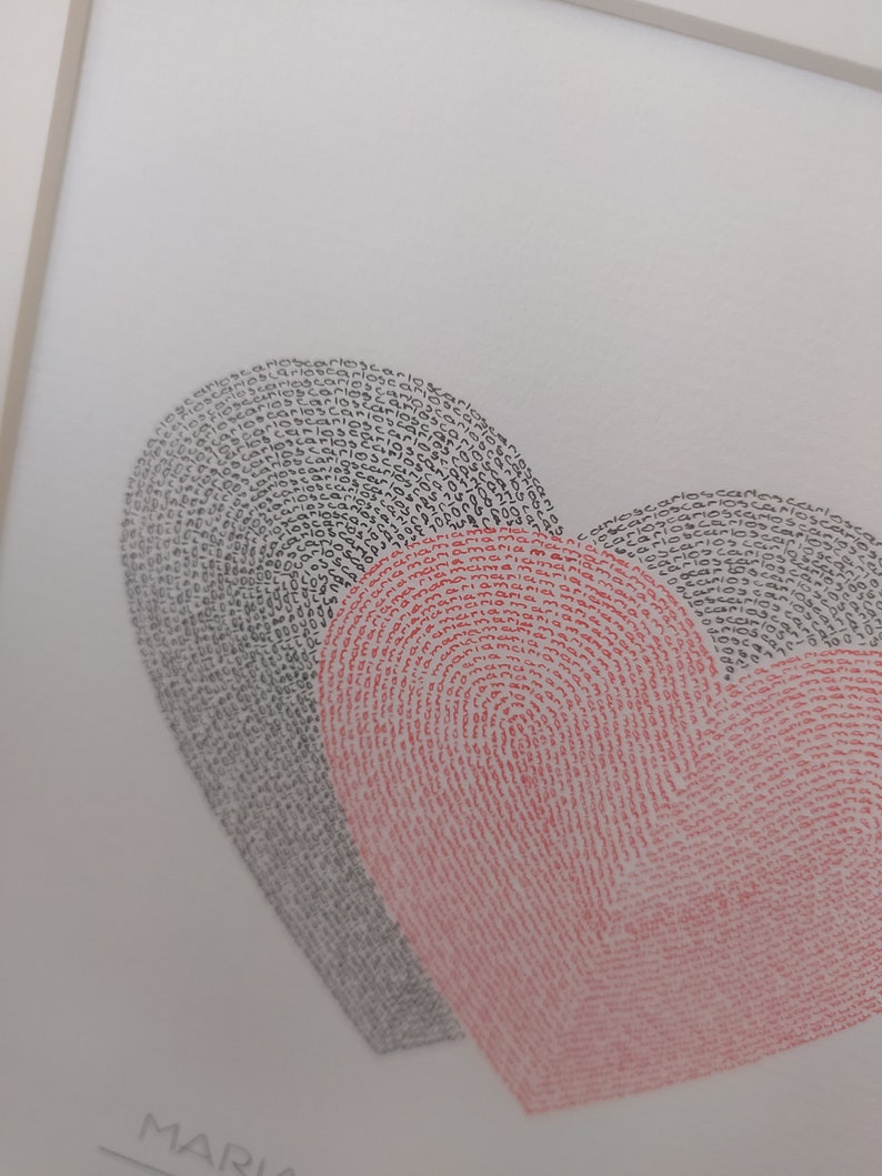 Op de afbeelding: Een ingelijste afbeelding met twee overlappende hartvormen gevormd door herhalende tekst. Het linkerhart is samengesteld uit het woord 'carlos' in zwarte inkt, terwijl het rechterhart is samengesteld uit het woord 'maria' in rode inkt op een witte achtergrond.