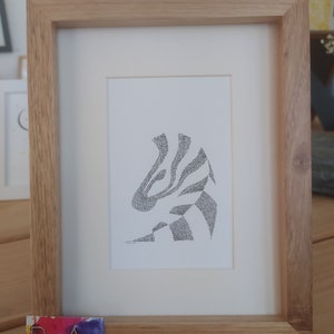May include: A framed black and white line art drawing of a zebra head, with the zebra's stripes created by a series of dots. The drawing is in a light wood frame.