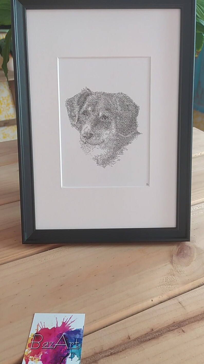 May include: A black and white framed print of a dog's face, created using a stippling technique. The print is on white paper and is framed in a black frame.