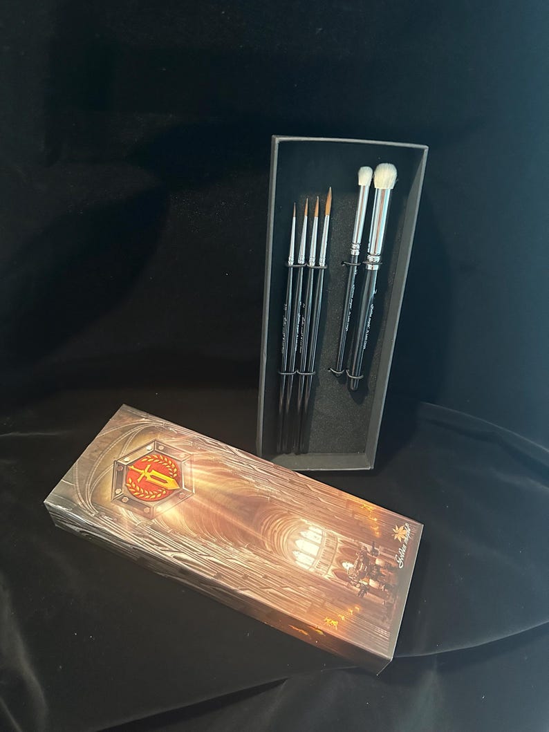 May include: A set of makeup brushes in a black box, with a matching box on the side. The brushes have black handles and silver ferrules. The box on the side has a gold and red emblem.