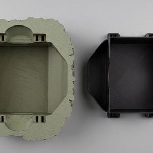 May include: A top-down view of two components: a sage green, textured, rock-like outer shell with a rectangular hollow center, and a separate black, smooth, rectangular insert with a notched side designed to fit within the outer shell.