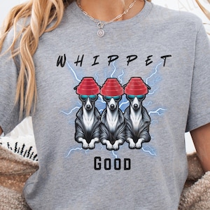 Könnte beinhalten: Graues T-Shirt mit einem Aufdruck von drei Whippet-Hunden mit roten Hüten und Sonnenbrillen, mit dem Wort "WHIPPET" darüber und "GOOD" darunter. Das Design beinhaltet blaue Blitze.