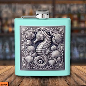 May include: Teal hip flask featuring a detailed seahorse and seashell design. The flask has a silver cap and a rectangular shape. The design is in a rectangular frame. The words "All Over Wild" are in the bottom left corner.
