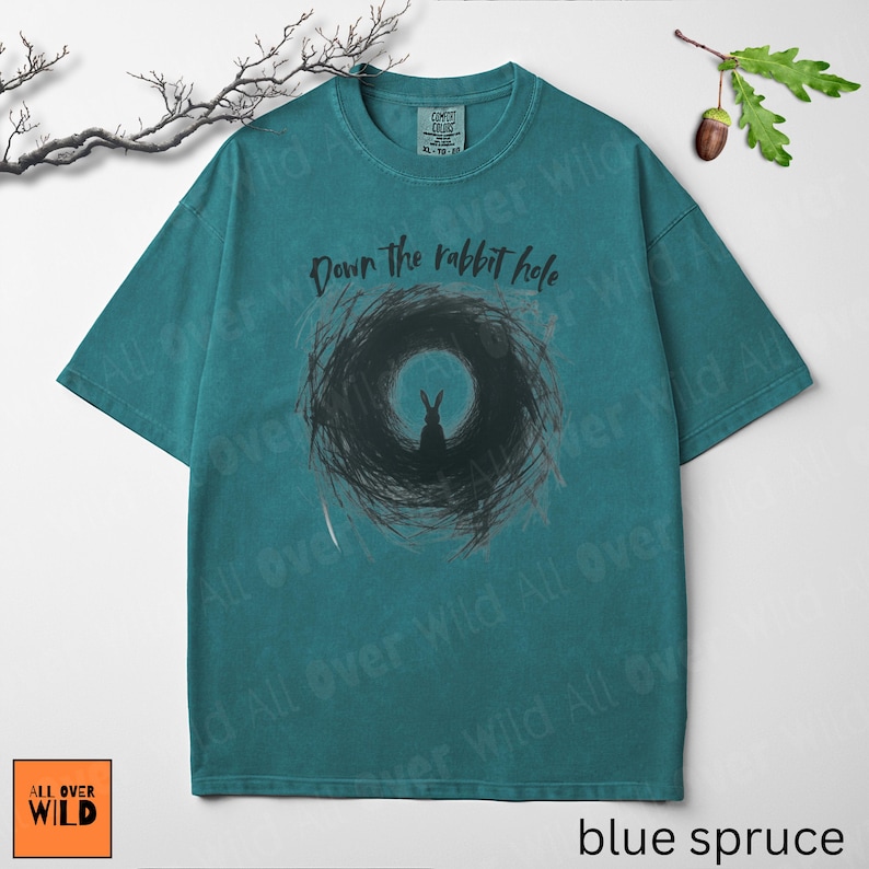 May include: Teal-coloured t-shirt featuring the phrase "Down the rabbit hole" above a rabbit graphic. The design is on a vintage-wash tee with a crew neck. The brand logo "All Over Wild" is in the bottom left corner. The shirt is a size XL.