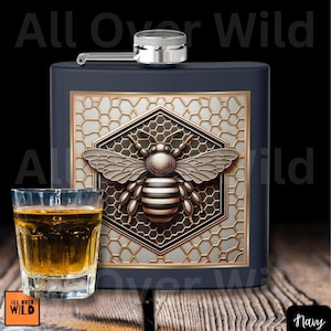 May include: Navy blue flask with a silver cap and a decorative bee design. The bee is centered on a honeycomb pattern. A shot glass with amber liquid sits in front of the flask.