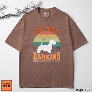 May include: A brown short-sleeved t-shirt featuring a graphic of a white dog silhouette against a sunset background. The text reads I'M NOT BARKING I'M EXPLAINING WHY I'M RIGHT. The shirt has a crew neckline and a distressed, washed-out fabric appearance.