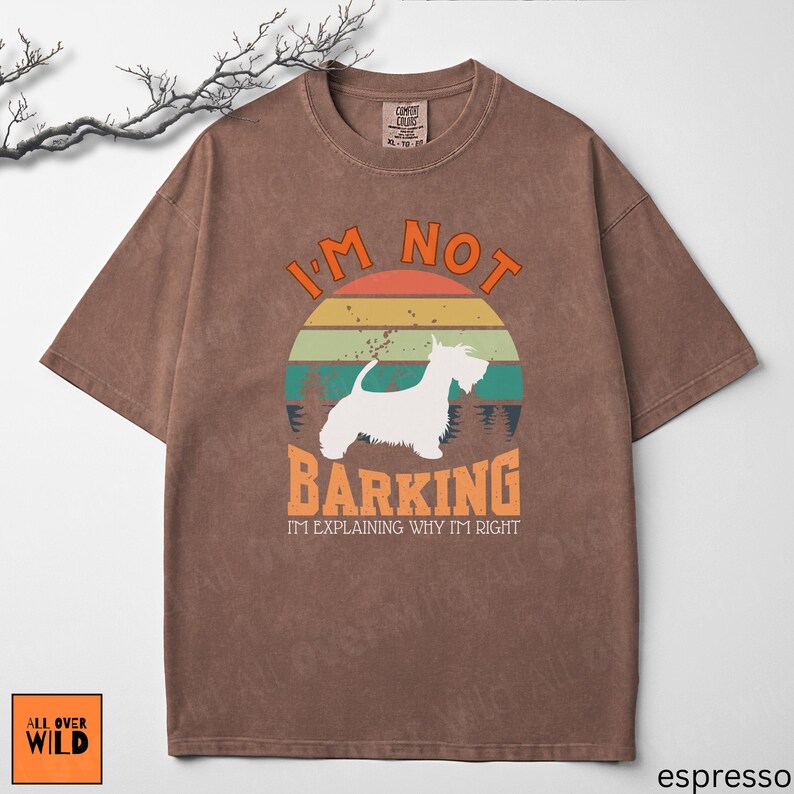 May include: A brown short-sleeved t-shirt featuring a graphic of a white dog silhouette against a sunset background. The text reads I'M NOT BARKING I'M EXPLAINING WHY I'M RIGHT. The shirt has a crew neckline and a distressed, washed-out fabric appearance.
