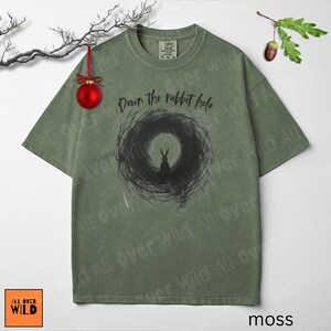 May include: A moss green t-shirt featuring the phrase "Down the rabbit hole" and a black rabbit graphic. The shirt has a crew neck and short sleeves. The brand logo is in the bottom left corner. The shirt is a comfortable fit.